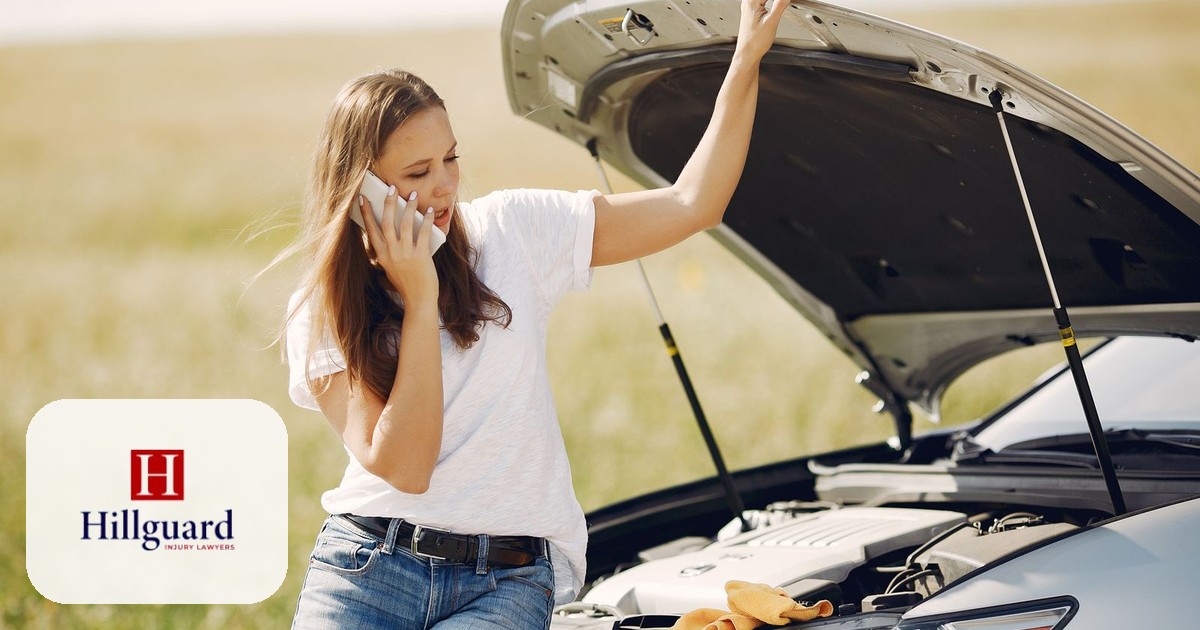 Driver on the phone calling for help beside a damaged vehicle after a car accident