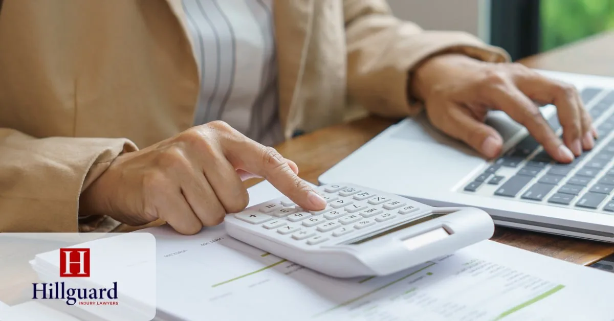 Calculating a personal injury lawyer’s net fee with a calculator, laptop, and financial documents after deductions